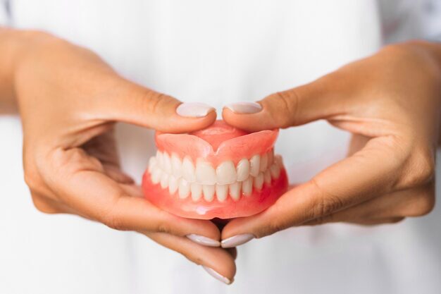 hands holding a complete upper and lower dental denture set.